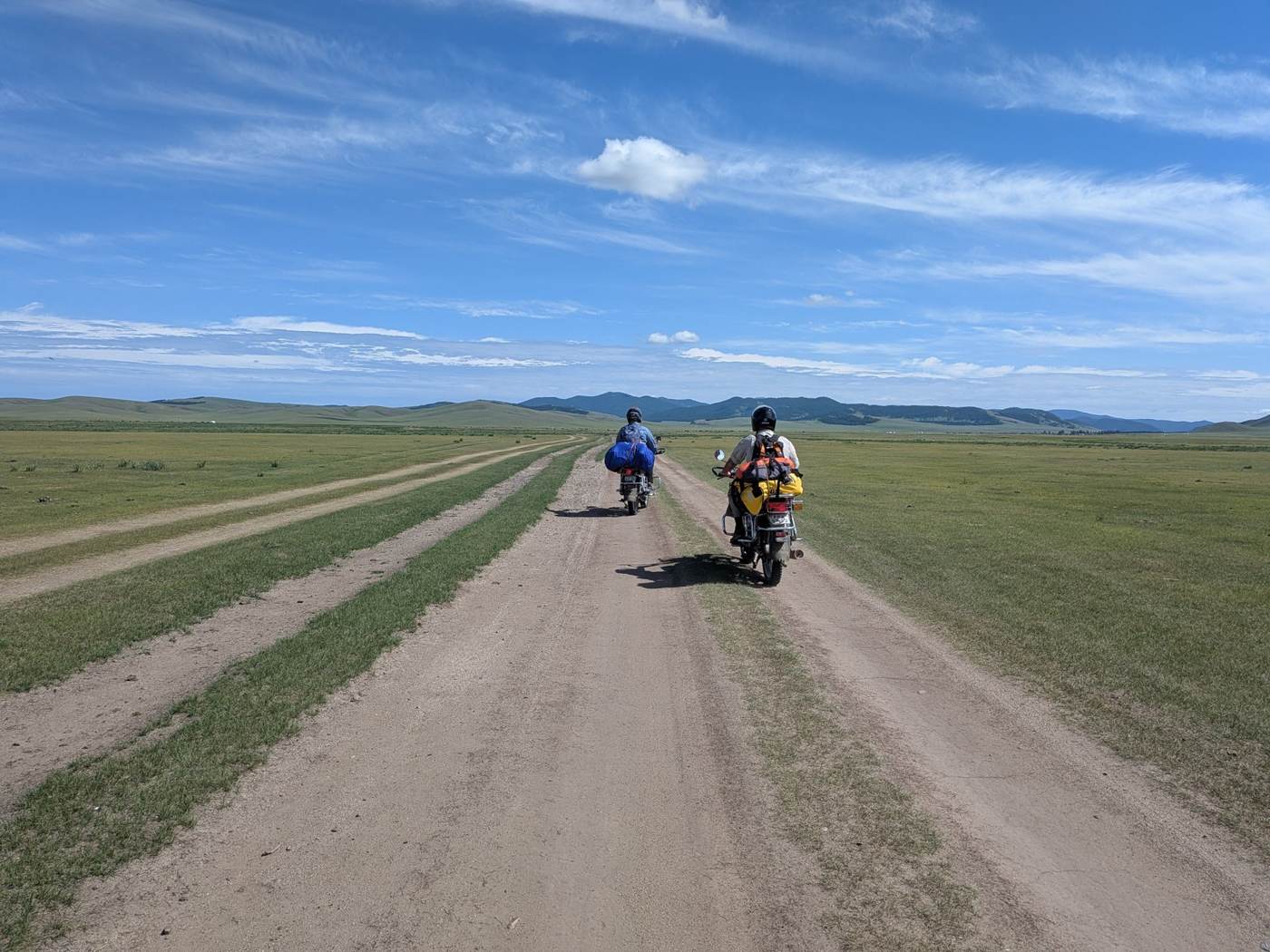Two riders on a dirt track across open steppe, Mongolia